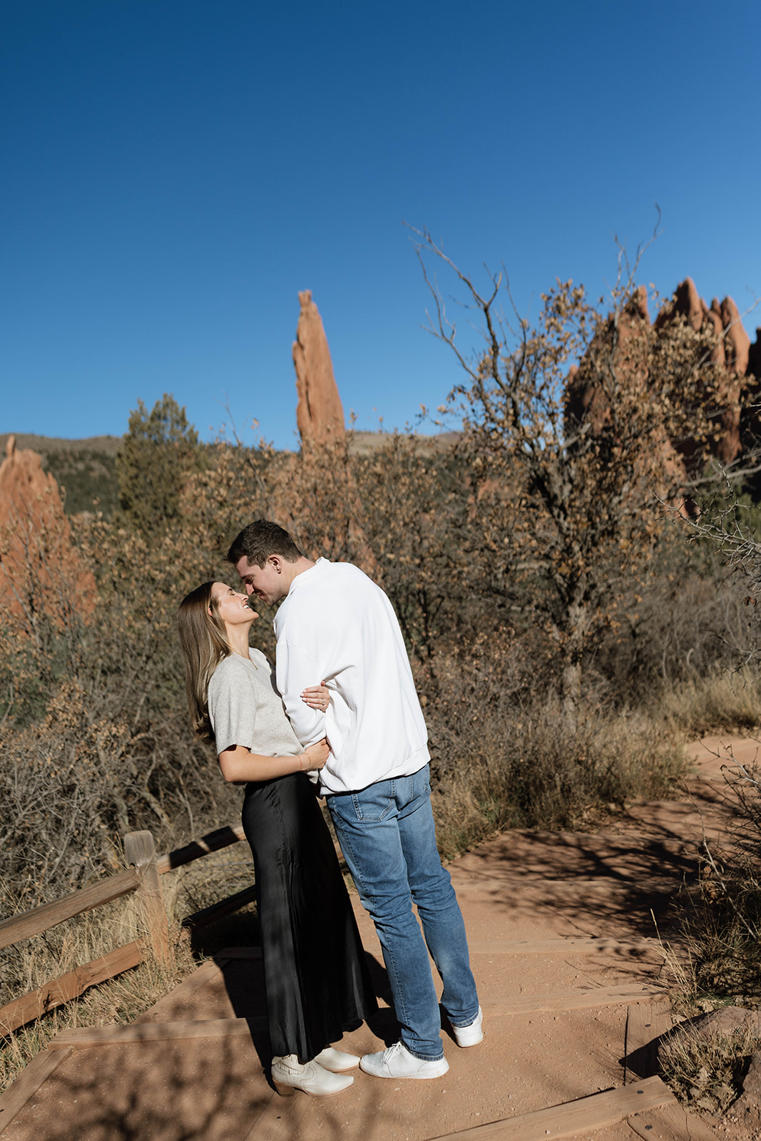 A close embrace between a couple as they kiss beside a stone overlook with soft morning light and layered desert cliffs in the distance.
