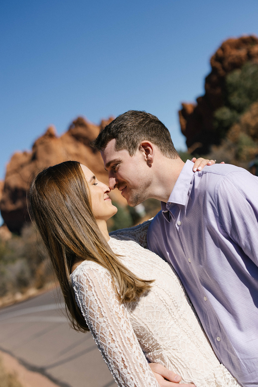 A close-up of a couple leaning in with their noses touching, smiling with red rock cliffs behind them.