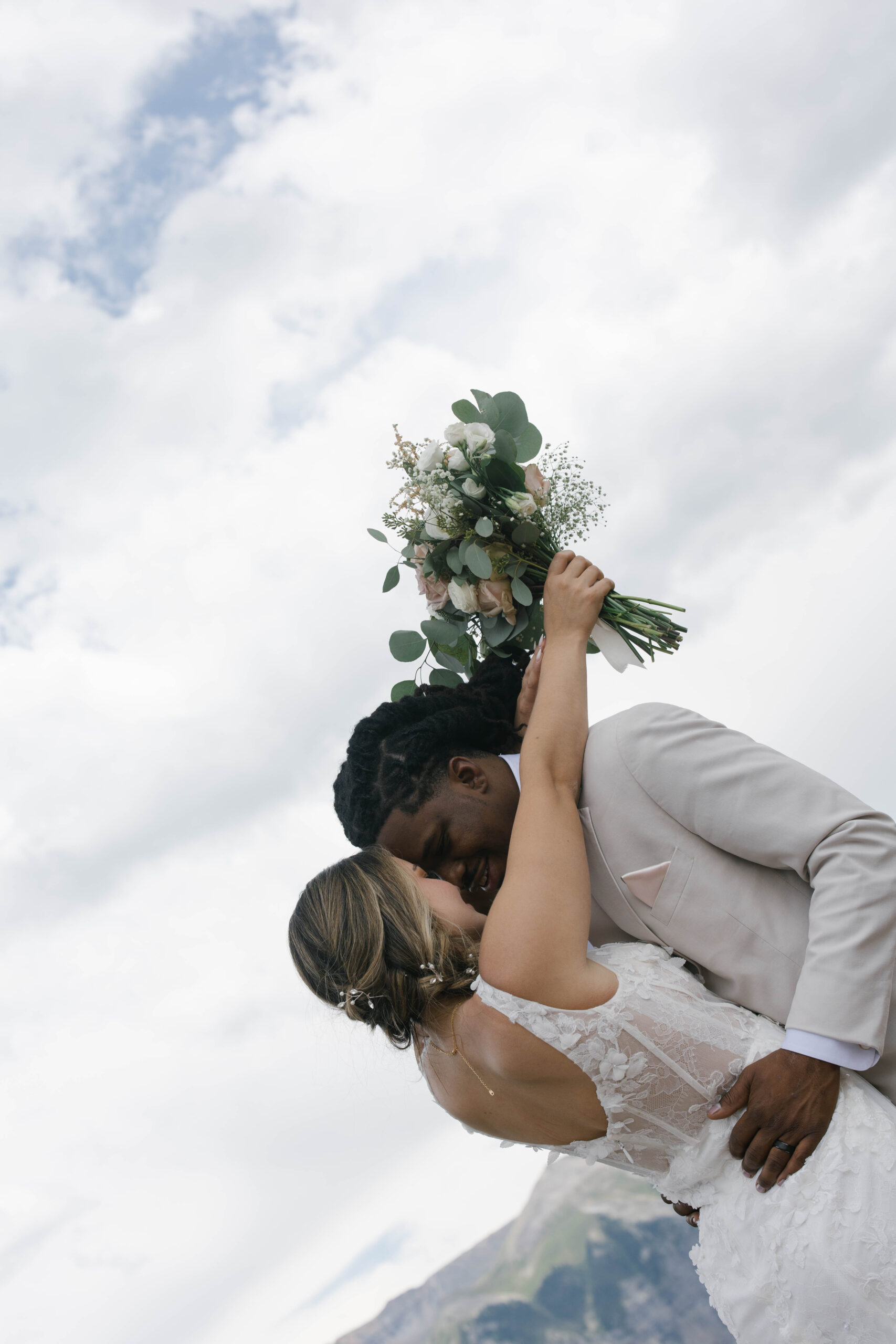 The bride laughing as she wraps her arms around the groom, lifting her bouquet toward the sky with sweeping mountain views in the background during their telluride elopement.