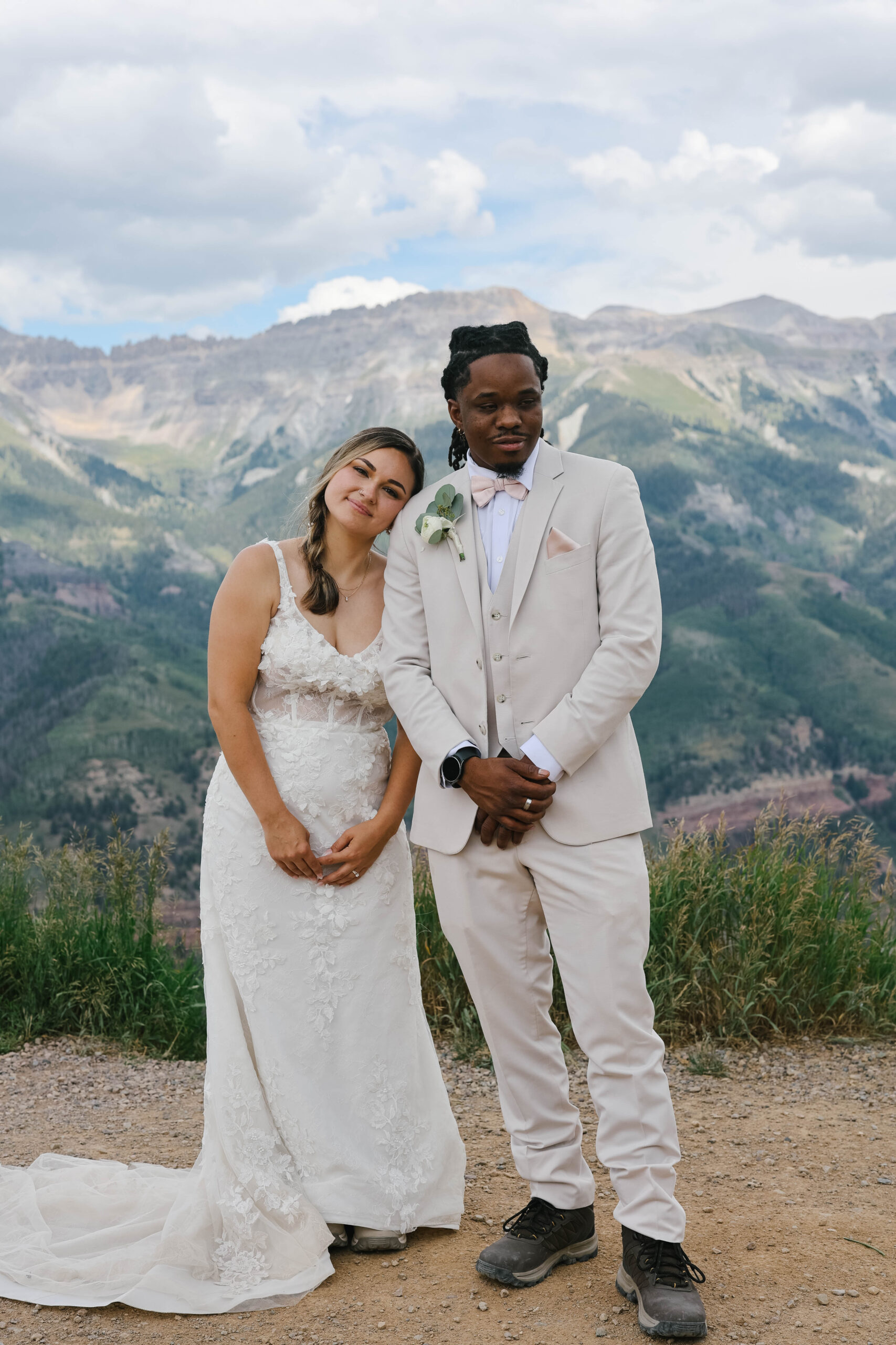 A bride resting her head on her groom’s shoulder as they smile softly with dramatic mountain peaks behind them during their telluride elopement.