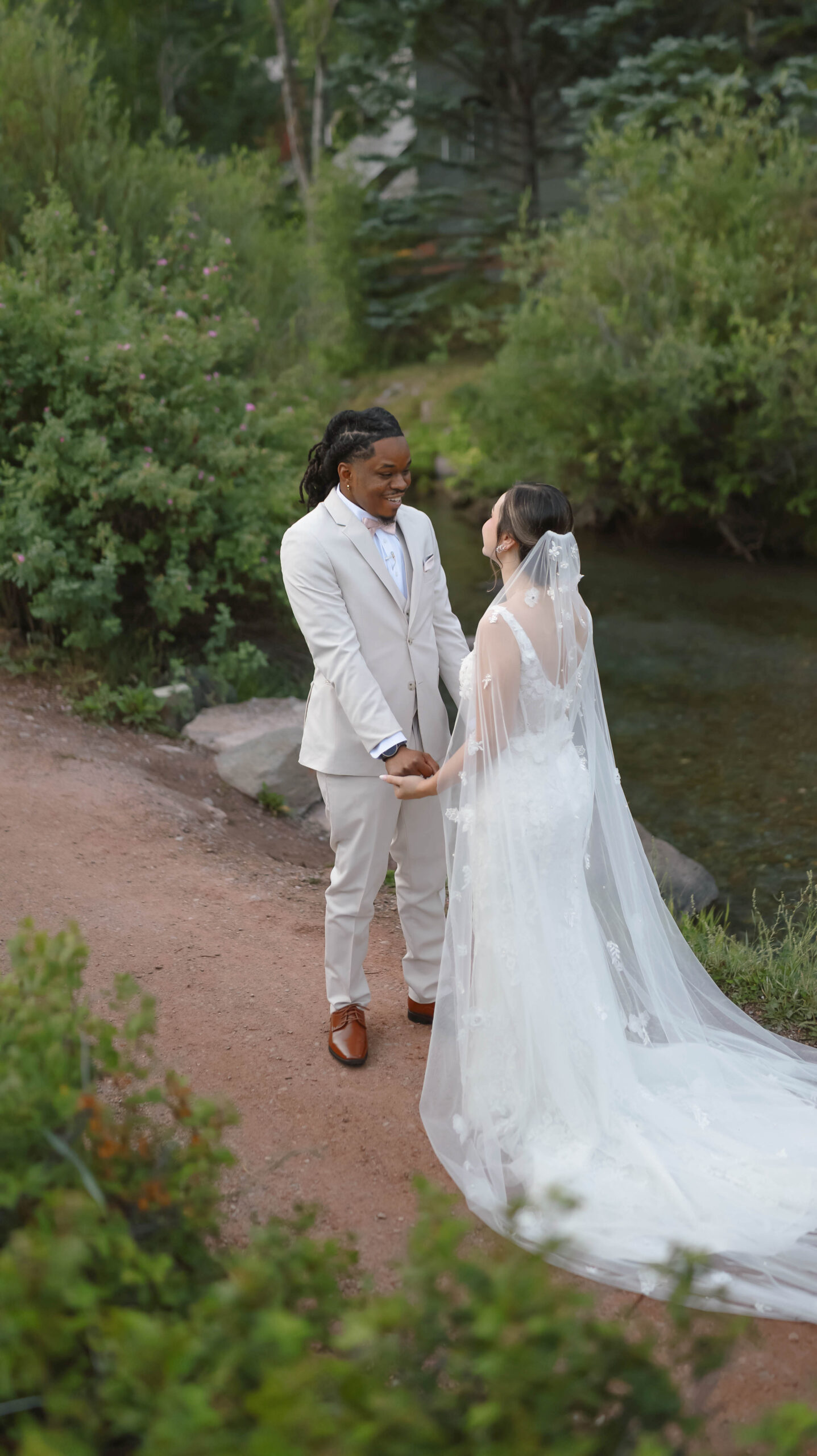 The couple smiling at each other beside a quiet riverside path, surrounded by lush greenery during their telluride elopement.