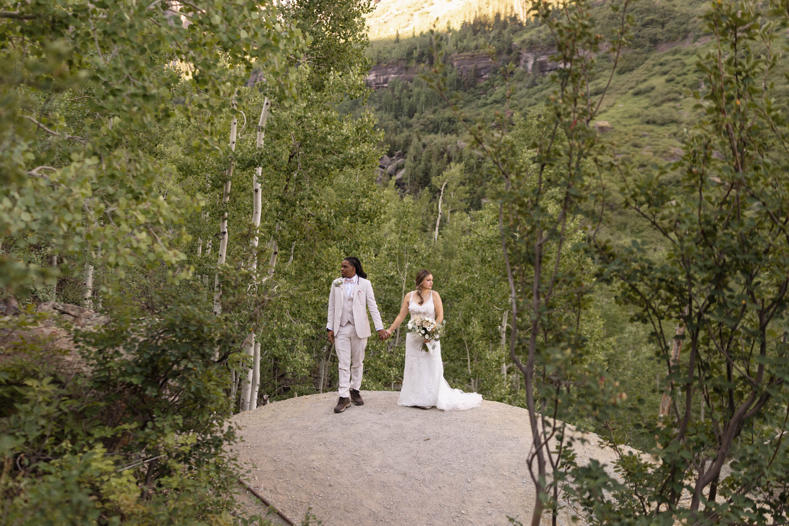The couple holding hands on a large boulder surrounded by aspens and mountain scenery during their telluride elopement.