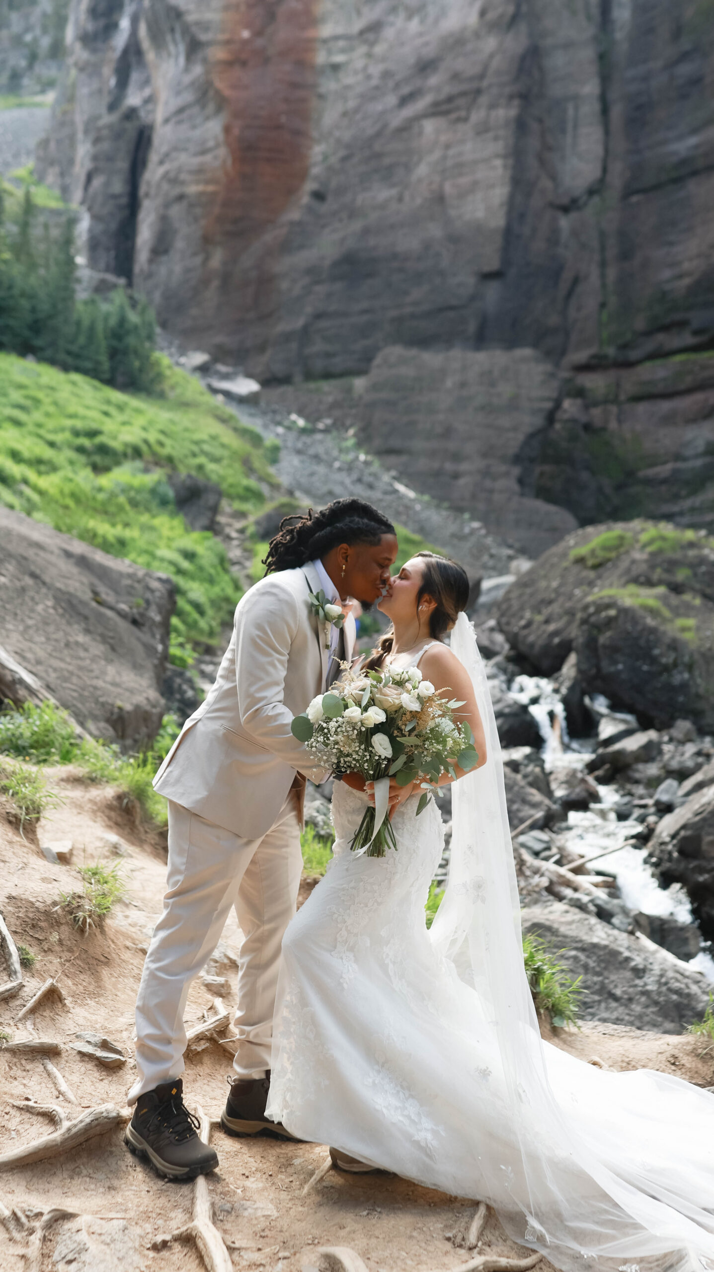 The couple sharing a kiss beside a cascading waterfall, the bride holding her bouquet close during their telluride elopement.