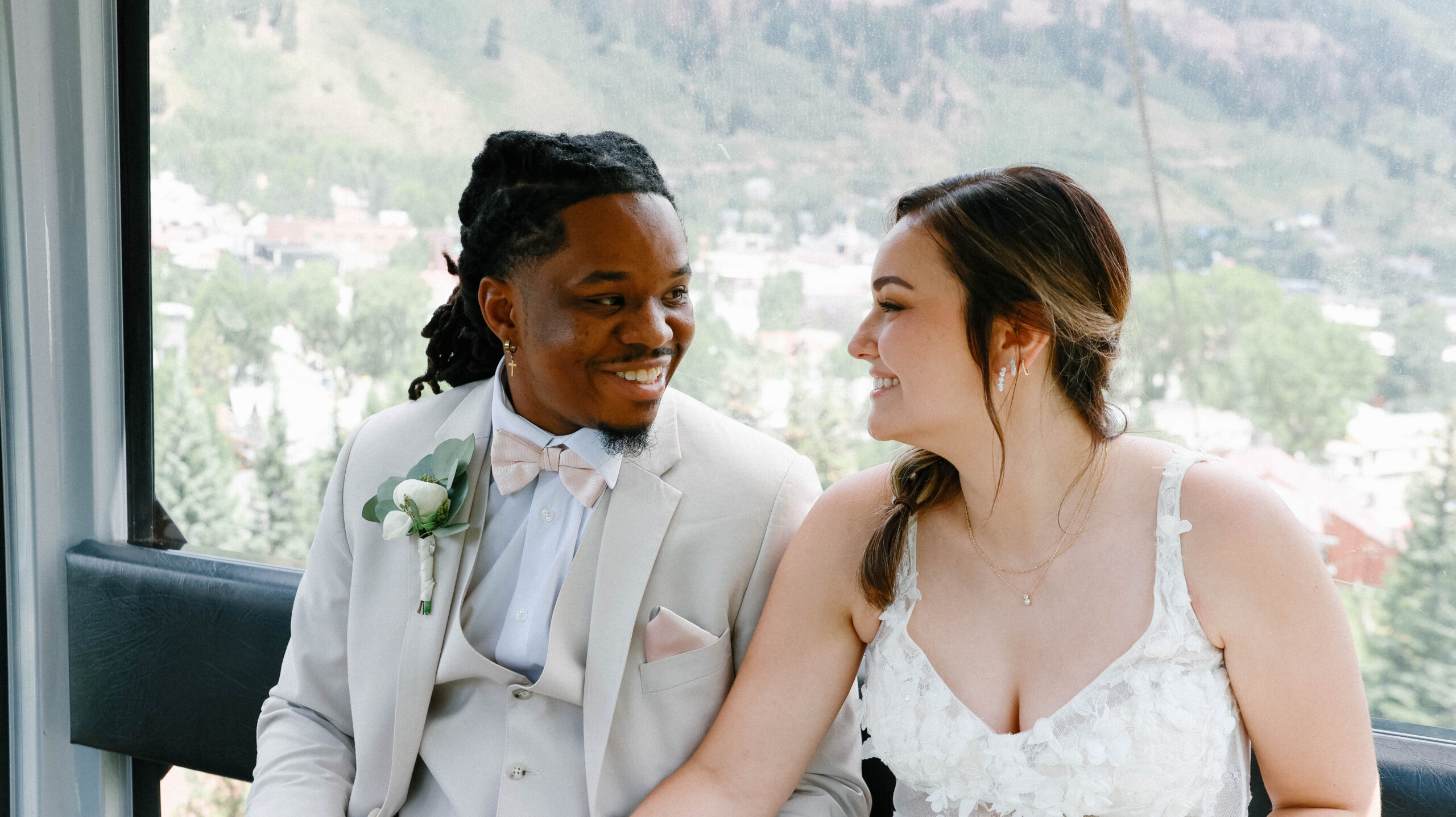 The bride and groom smiling at each other inside the gondola, with Telluride village and mountain scenery visible through the windows during their telluride elopement.