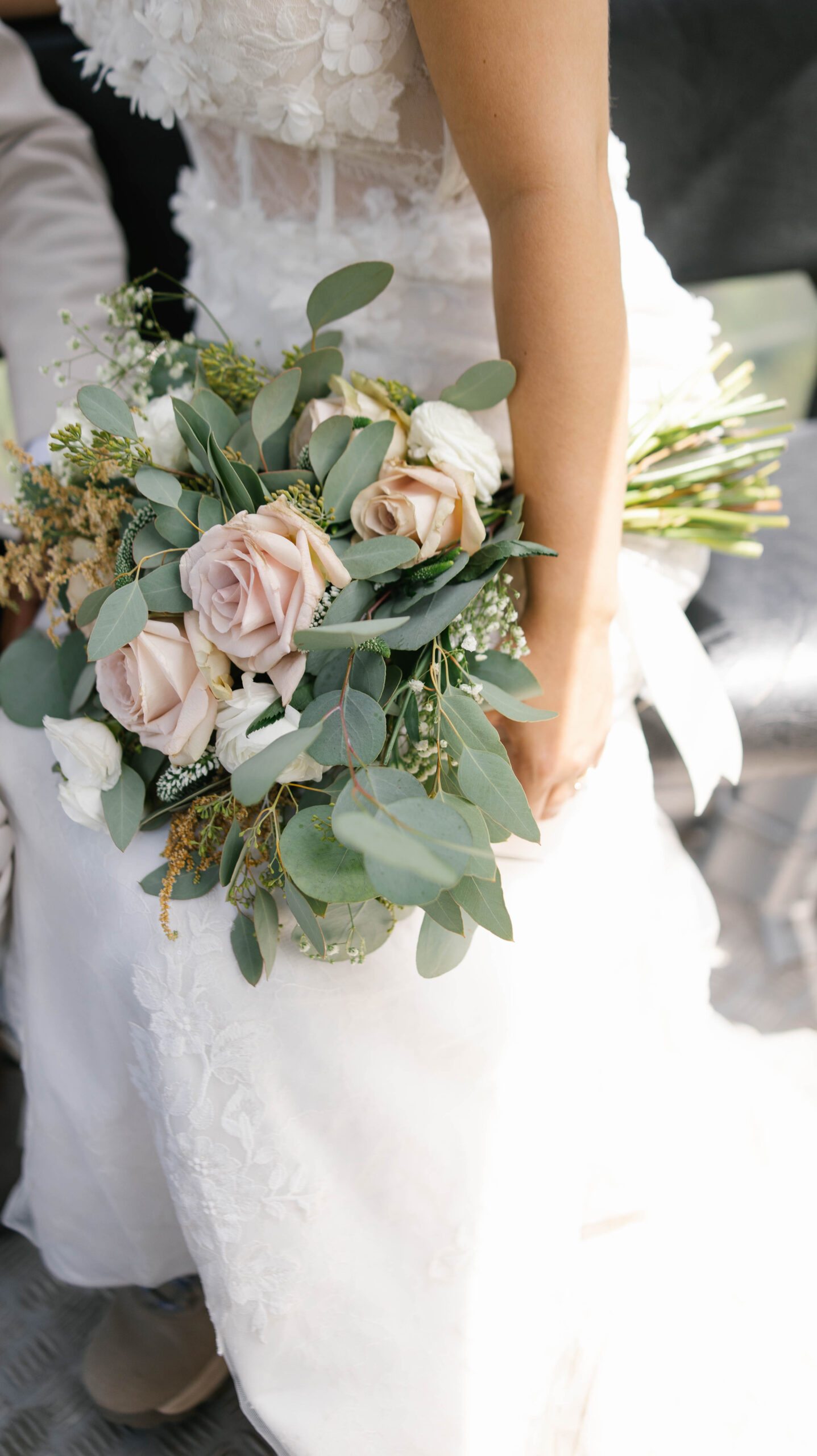 A close-up of the bride holding a soft, romantic bouquet of blush roses, white blooms, and eucalyptus while sunlight filters across her lace gown during their telluride elopement.