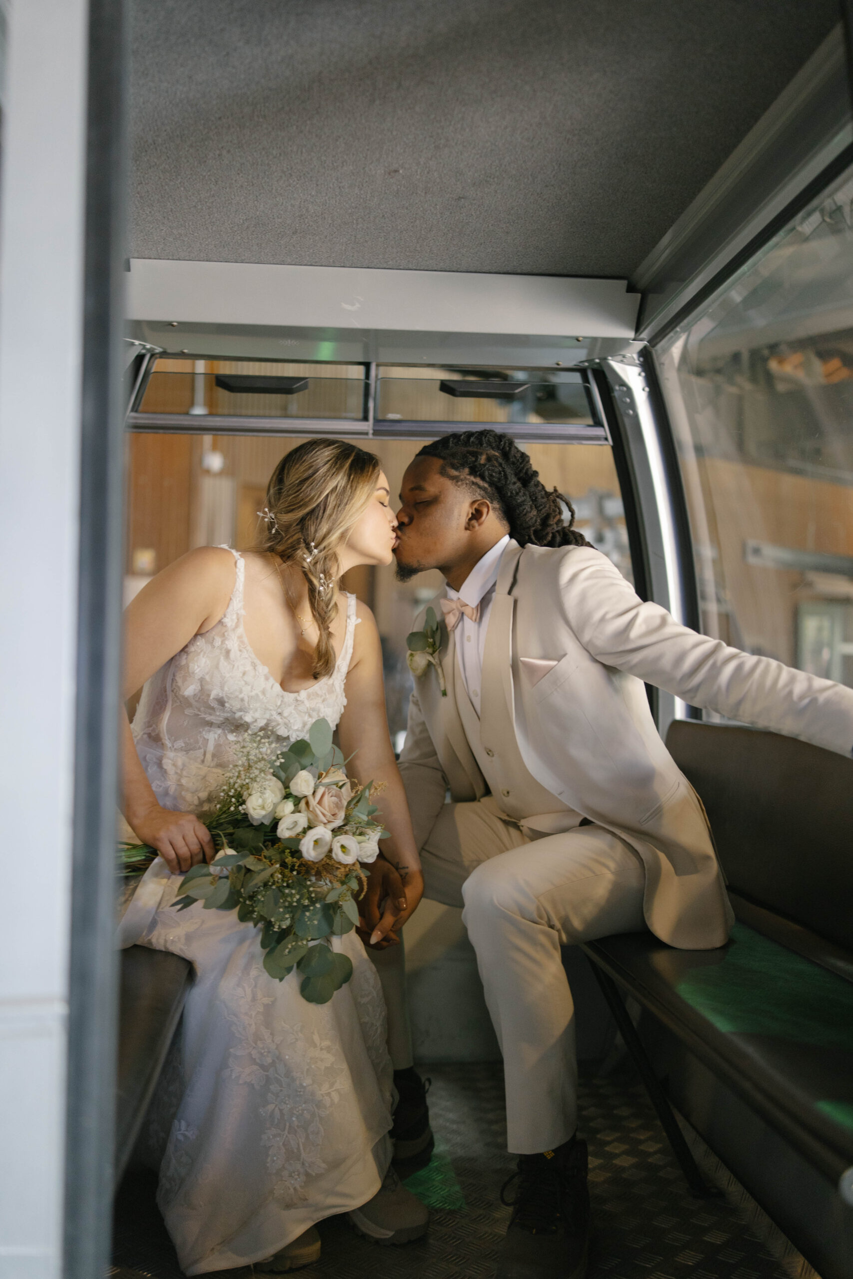 A romantic moment inside the gondola as the couple leans in for a kiss, holding the bride’s bouquet between them.