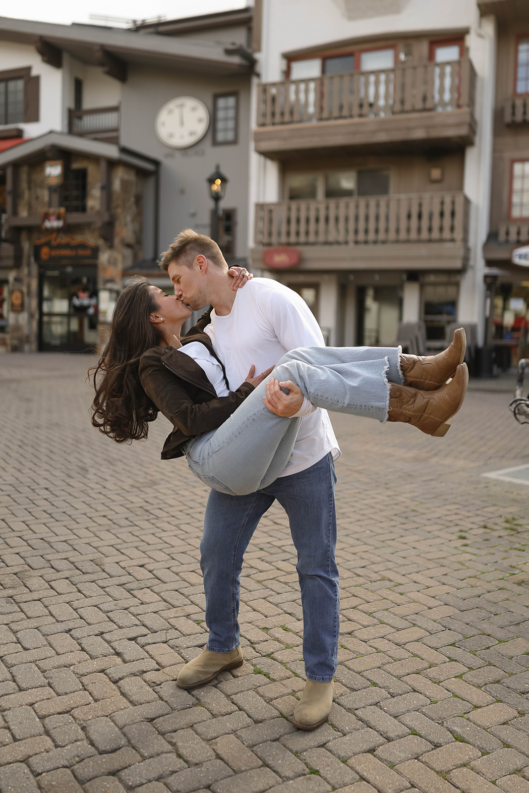 Playful engagement photo of a man lifting his partner in his arms for a kiss in the heart of vail village, colorado.