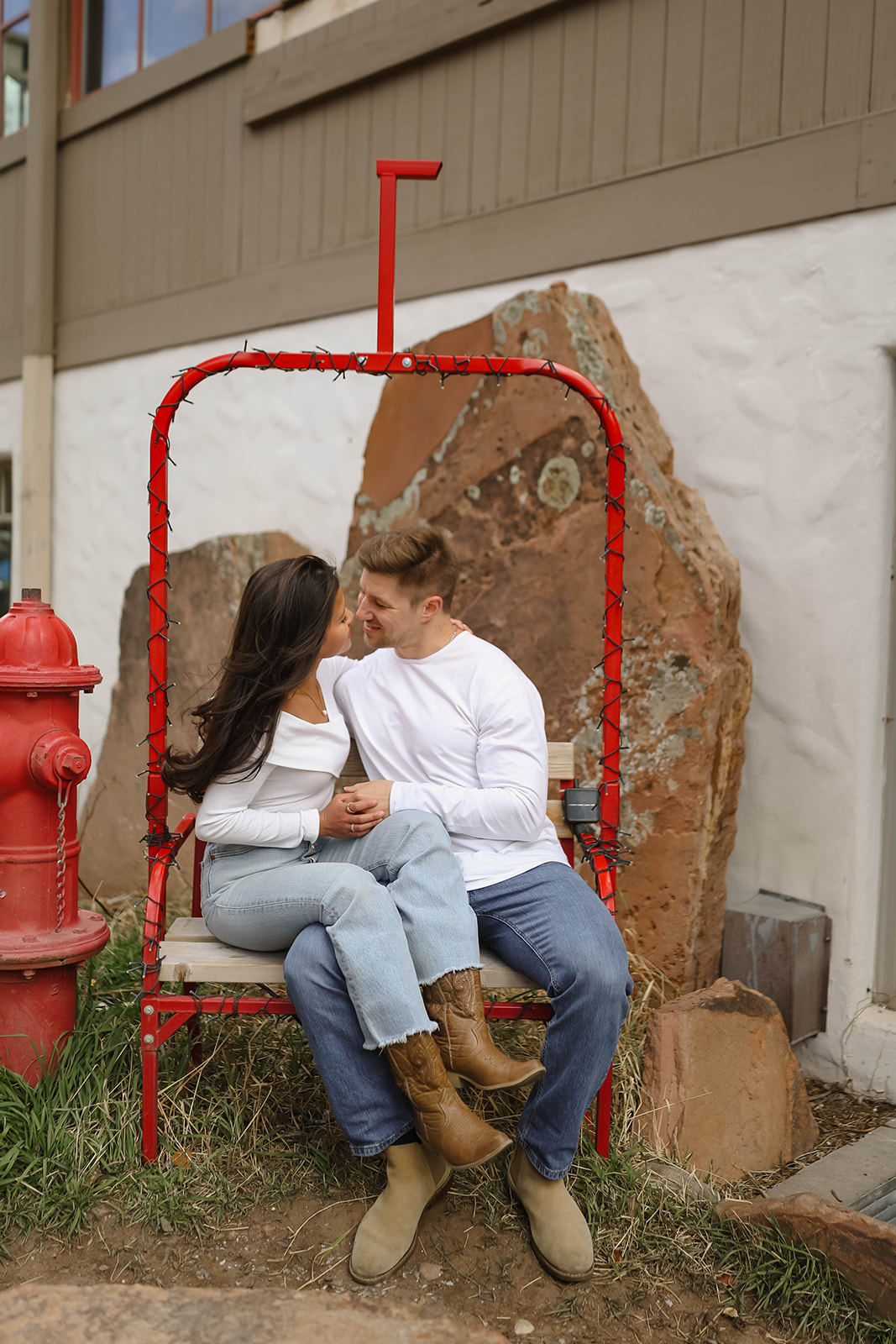 Cozy couple sitting together on a red chair bench near a fire hydrant and stone building in vail village, colorado.