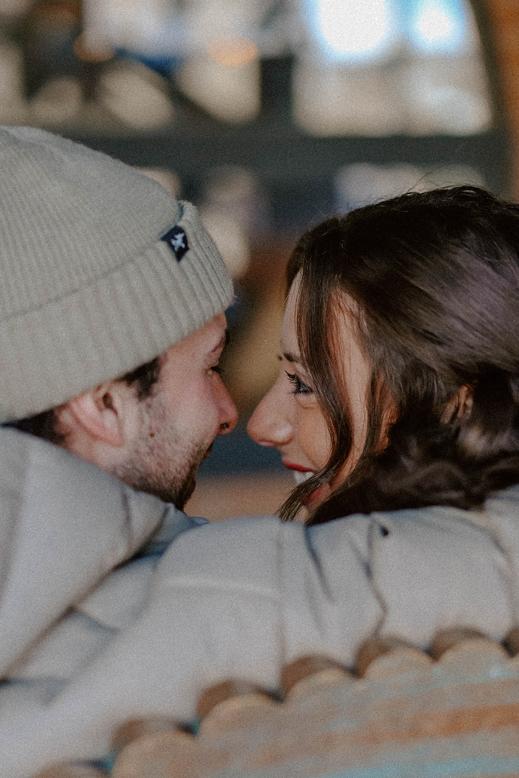 Close-up of a couple wrapped in winter jackets, gazing into each other’s eyes during a snowy mountain engagement session.