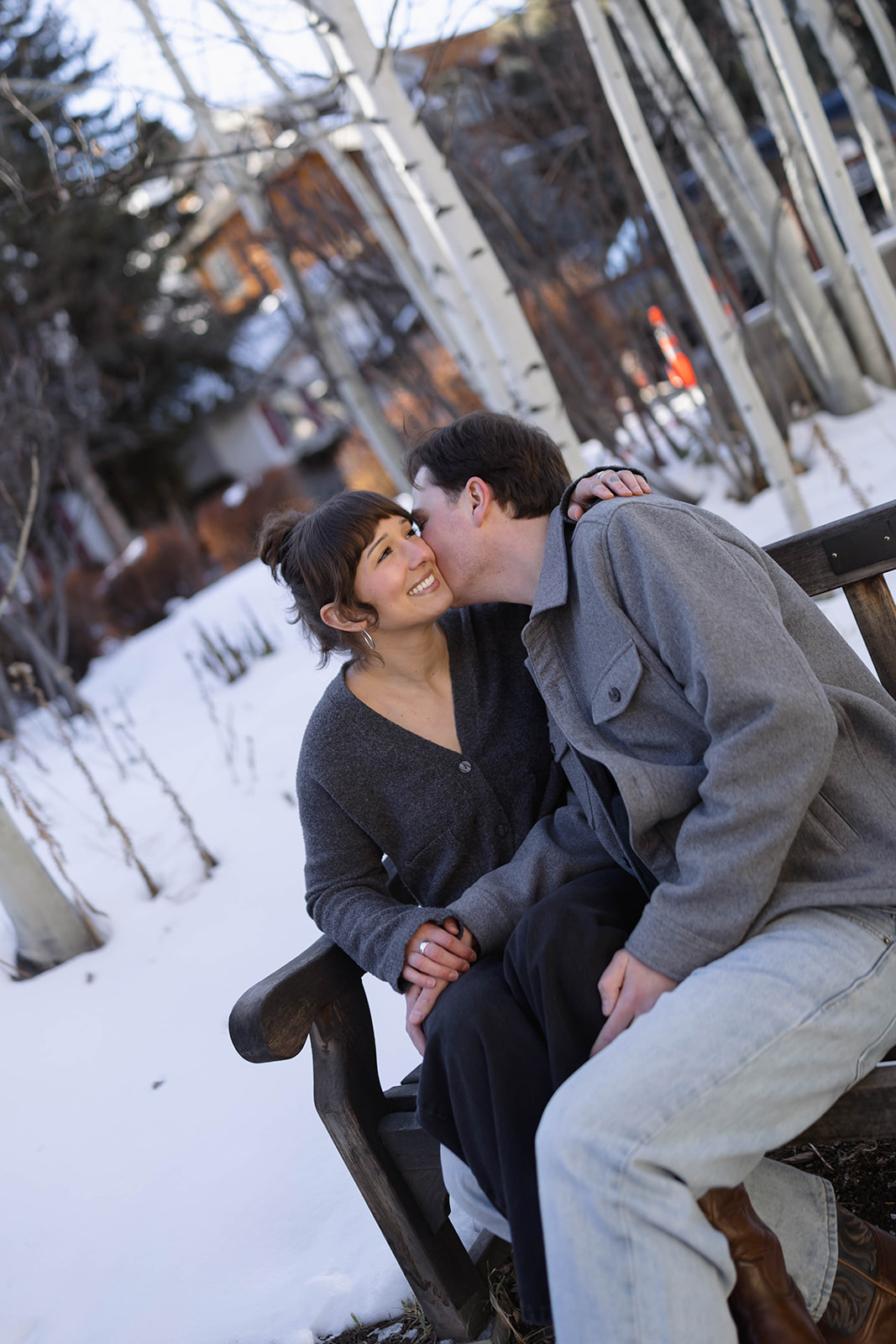 Winter engagement photo of a couple sharing a quiet kiss among snowy aspen trees in the Colorado mountains.