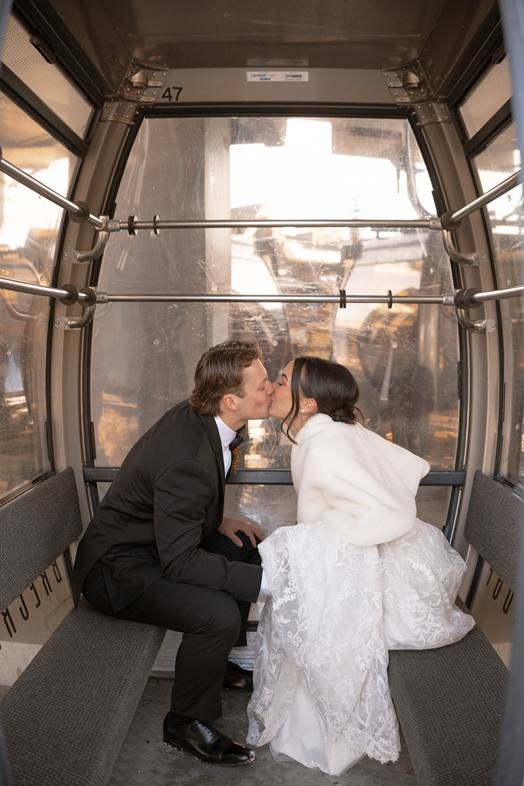 Bride and groom sharing a kiss in a ski gondola, winter mountain light glowing through the windows during their Breckenridge elopement.
