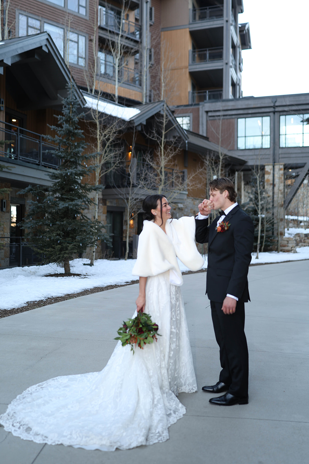 Bride and groom standing together in a snowy mountain village plaza, the bride holding a bouquet while wearing a white shawl during their Breckenridge elopement.