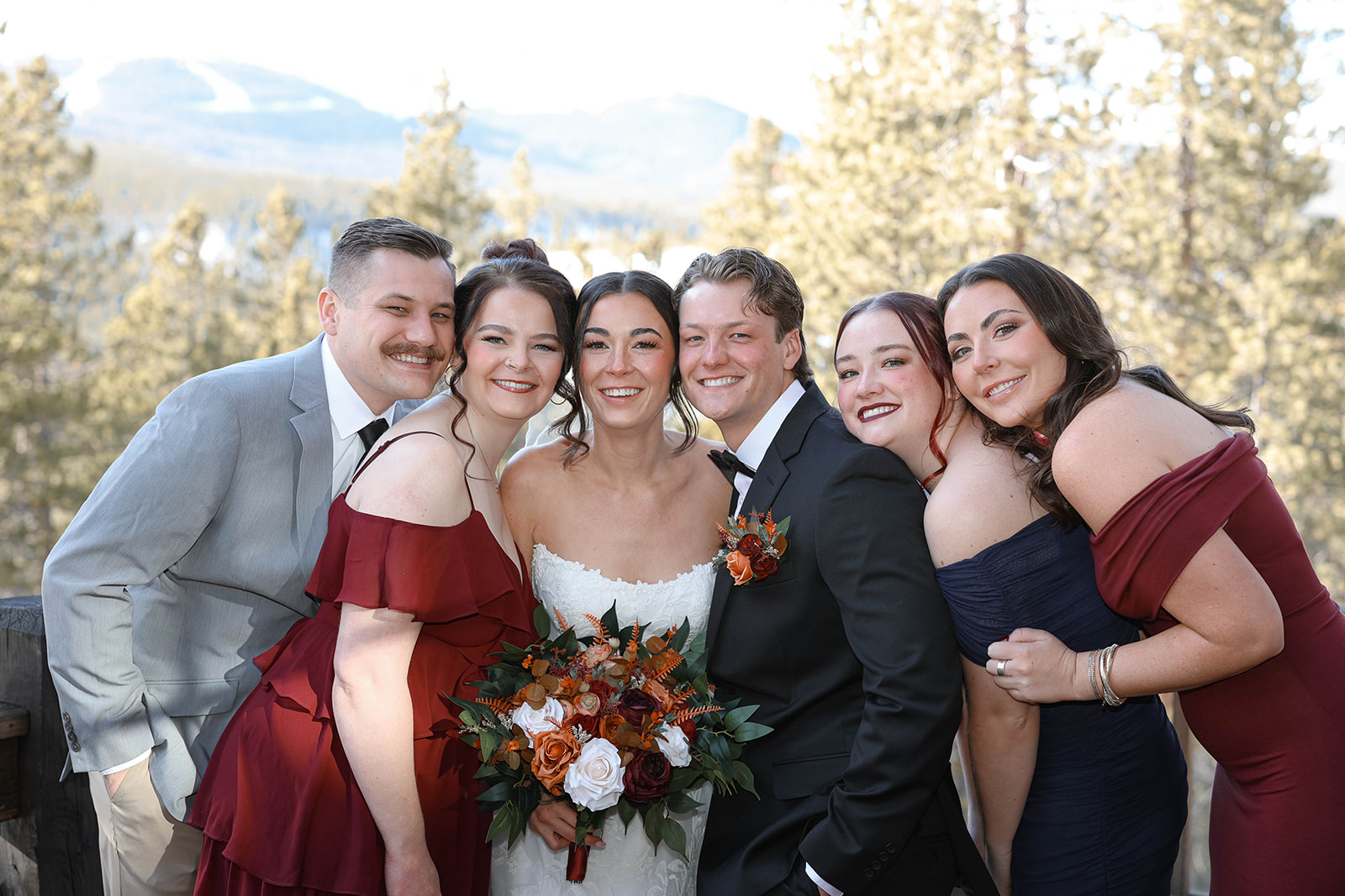 Wedding party posing outdoors together in winter attire, the bride centered holding a full bouquet of roses, pampas, and terracotta blooms, a celebratory Breckenridge elopement photo.