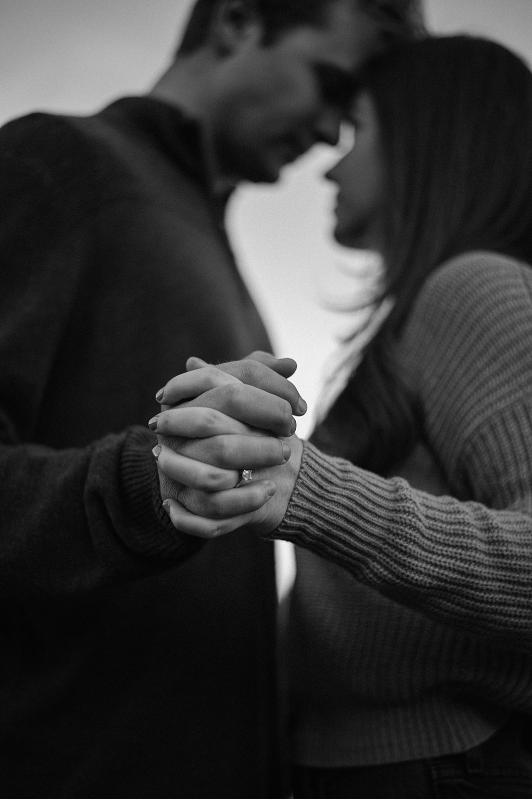 Black and white photo of a woman’s hands resting on her partner’s shoulders, showing an engagement ring after an intimate mountain proposal.