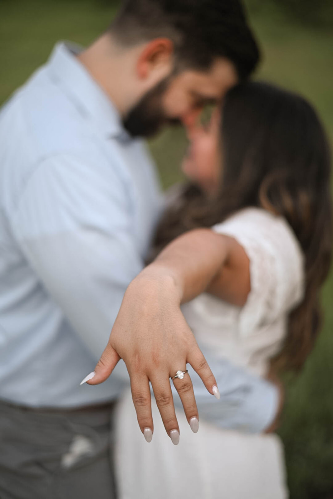 Close-up of an engagement ring on an outstretched hand with the couple blurred behind, photographed during a mountain proposal session.