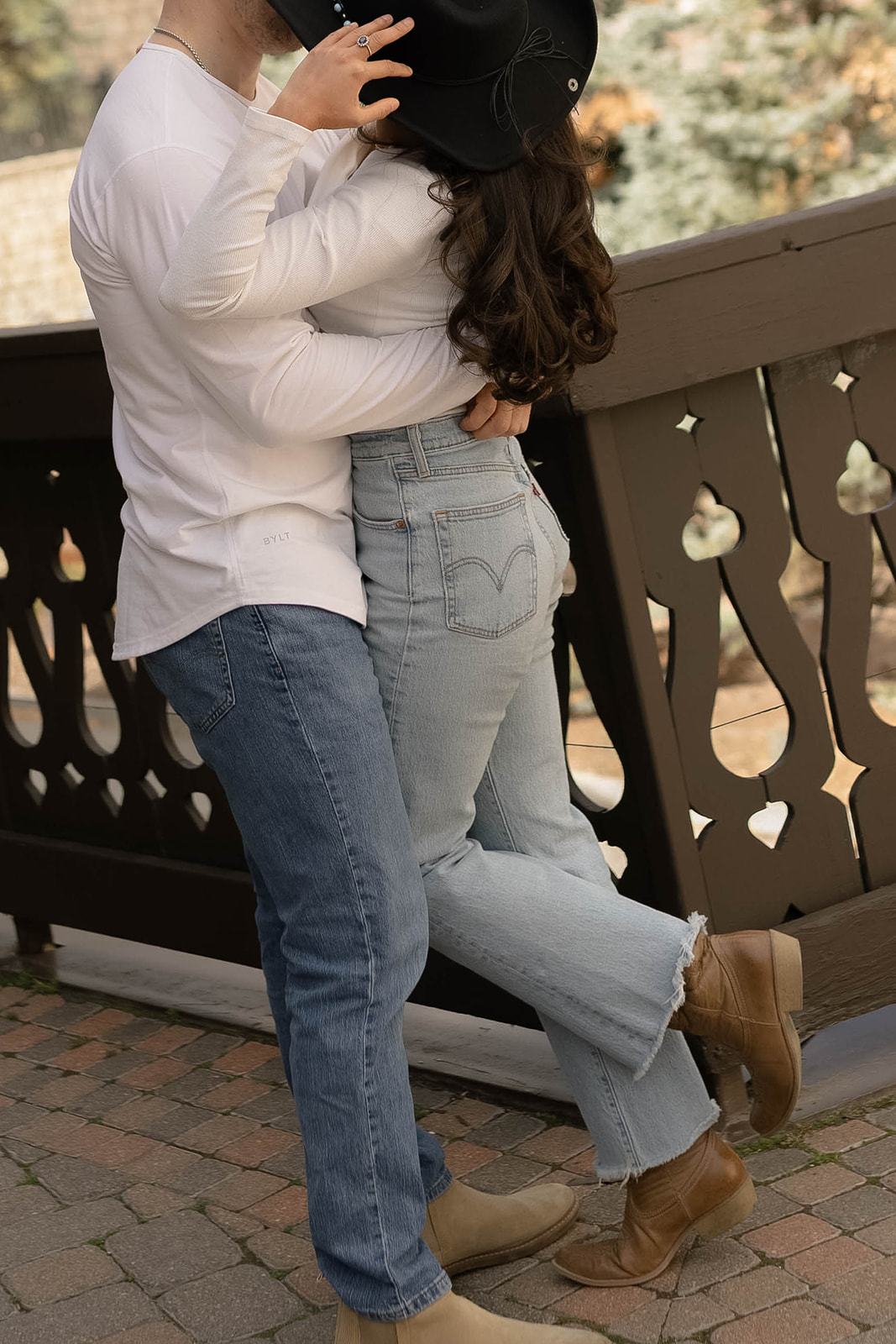 Close-up of a couple embracing near a decorative railing, focusing on their jeans and white tops while they lean into each other.