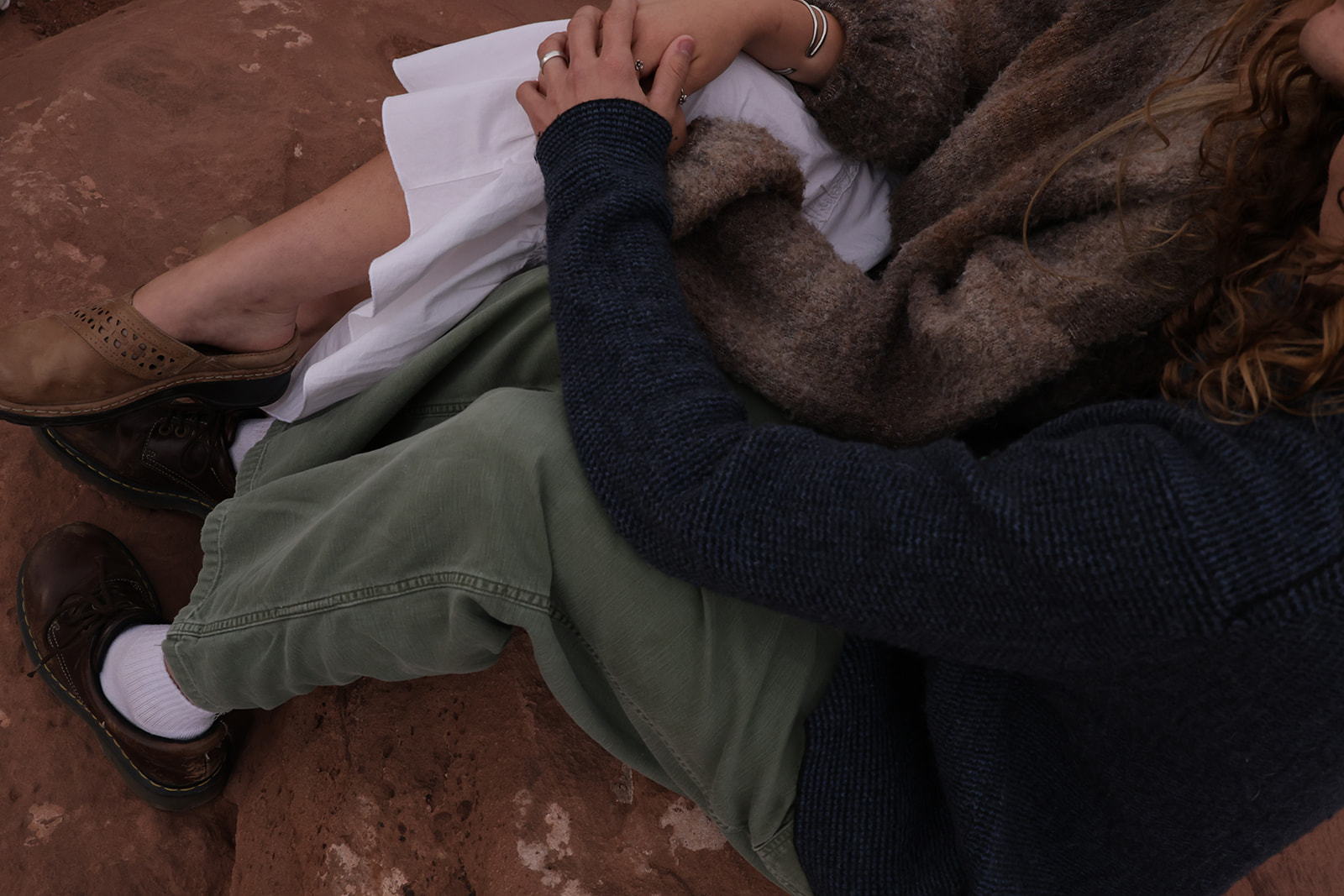 Close-up detail of intertwined legs and hands as a couple relaxes on red rock, highlighting texture, layers, and earthy tones ideal for outdoor couples outfit ideas.