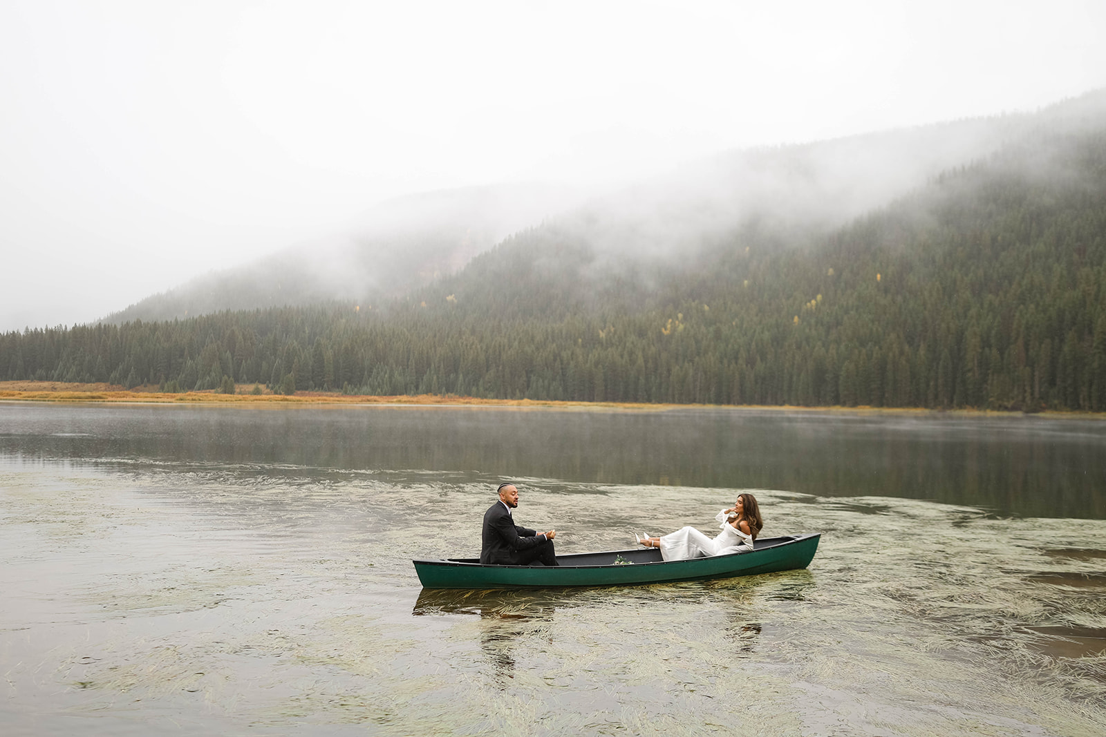 Foggy mountain lake scene with a couple sitting in a canoe, exchanging vows in the middle of the water during a romantic and secluded vail elopement.