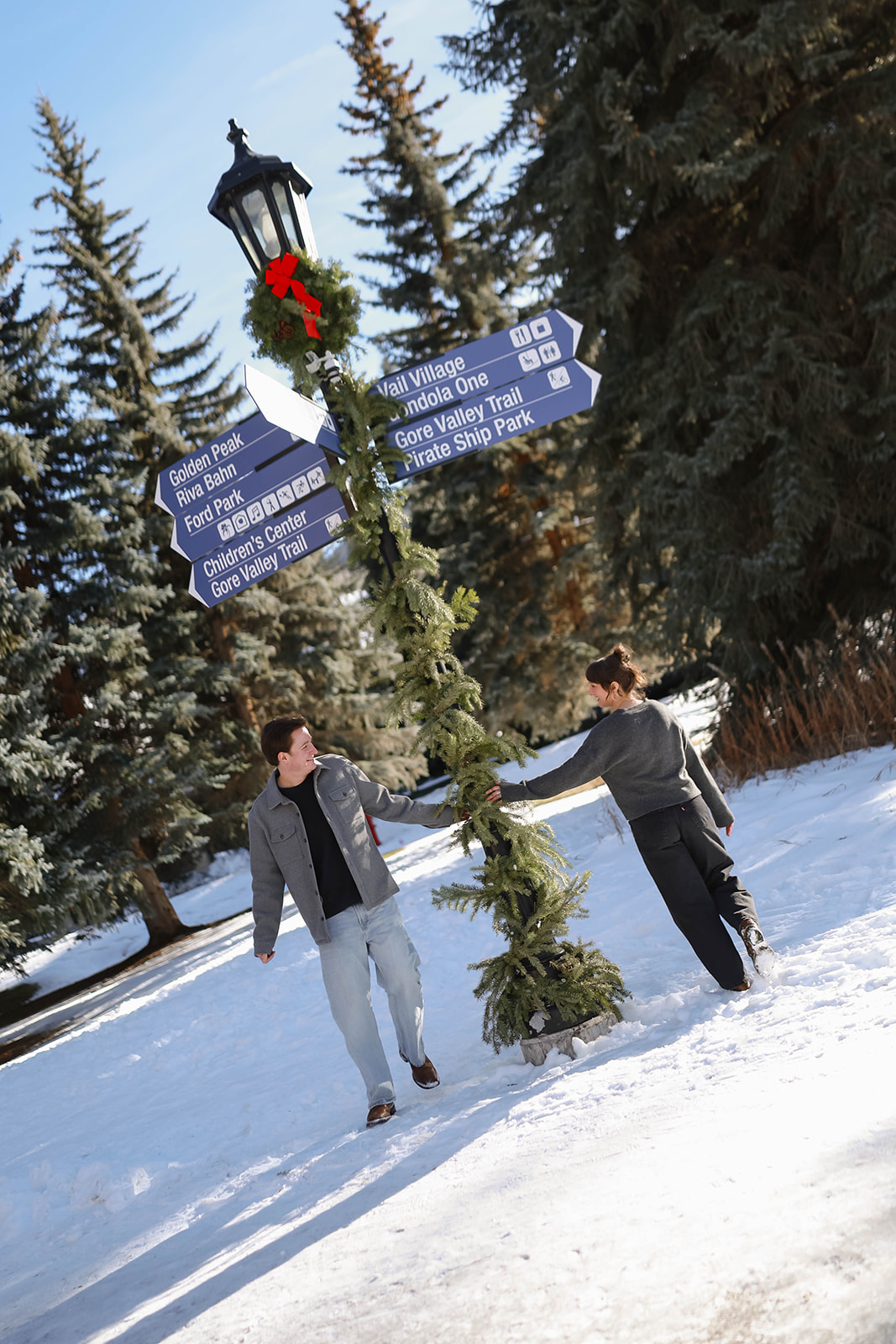 Couple walking hand-in-hand through snow near a decorated signpost in Vail Village, capturing a playful winter Vail elopement moment.