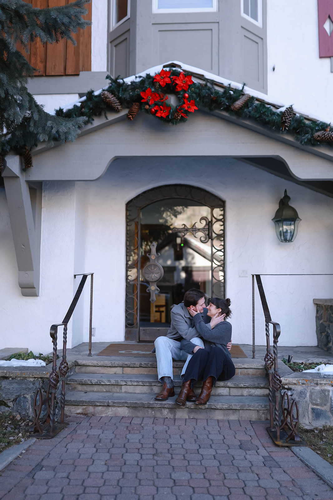 A couple sitting together on stone steps outside a decorated alpine building, sharing a cozy moment during their vail elopement in the village.