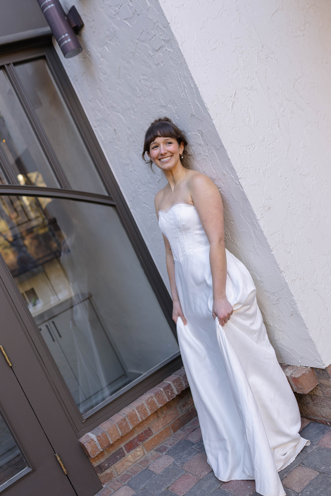 Bride smiling while standing against a textured wall in a simple strapless wedding dress during a relaxed vail elopement portrait.
