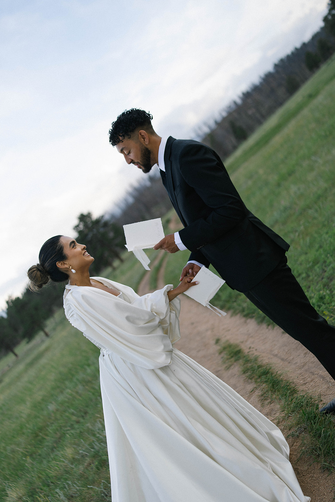 Couple reading handwritten vows to each other on a winding trail surrounded by open grass fields and soft mountain light.