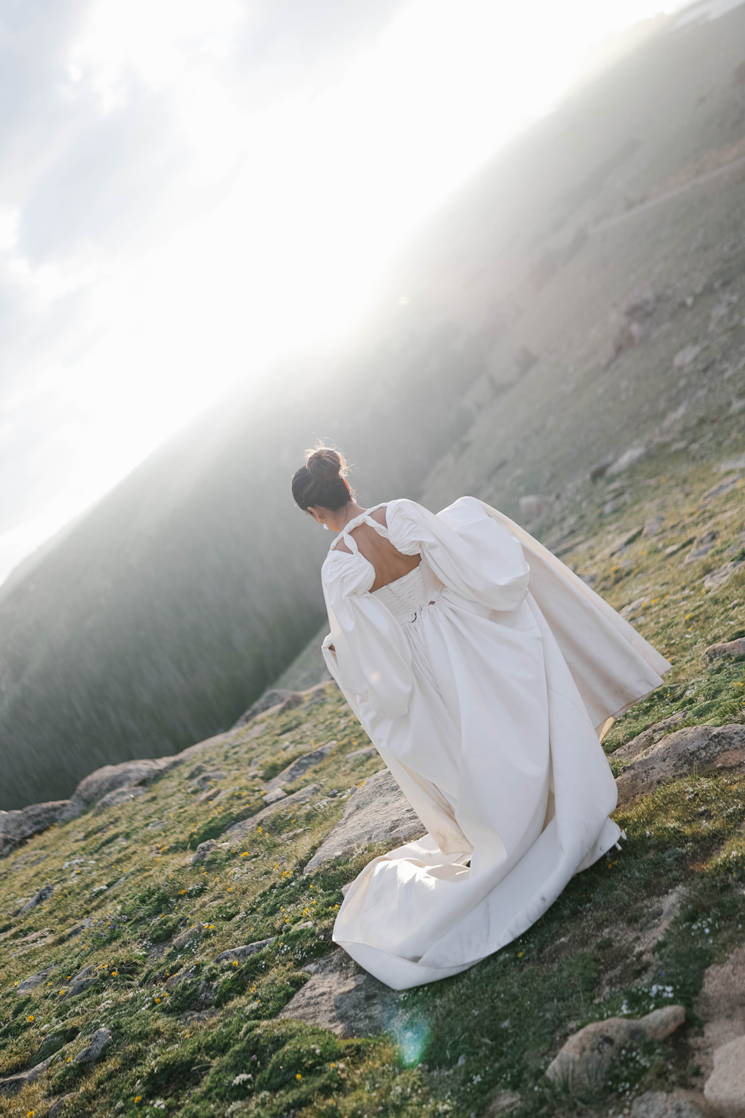 Bride walking across an alpine hillside at sunset, her gown catching golden light during a Rocky Mountain National Park Elopement.