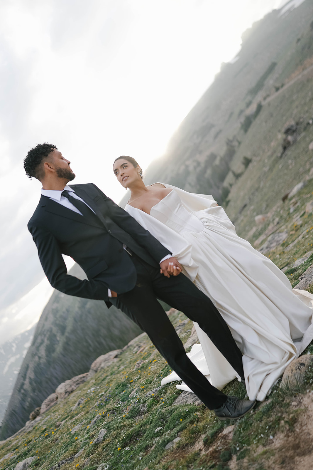 Close-up of bride and groom standing together on a mountaintop overlook, holding hands with sweeping alpine views behind them during a romantic Rocky Mountain National Park Elopement.