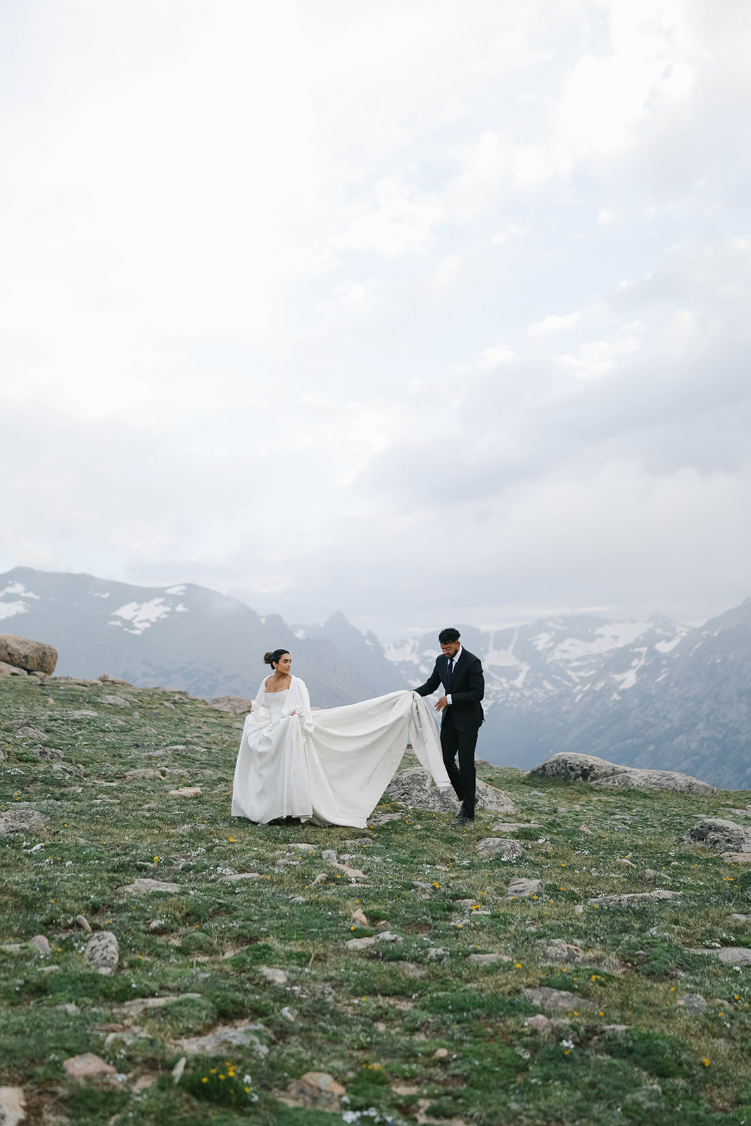 Bride and groom walking across an alpine tundra landscape with snow-capped peaks during their Rocky Mountain National Park Elopement.