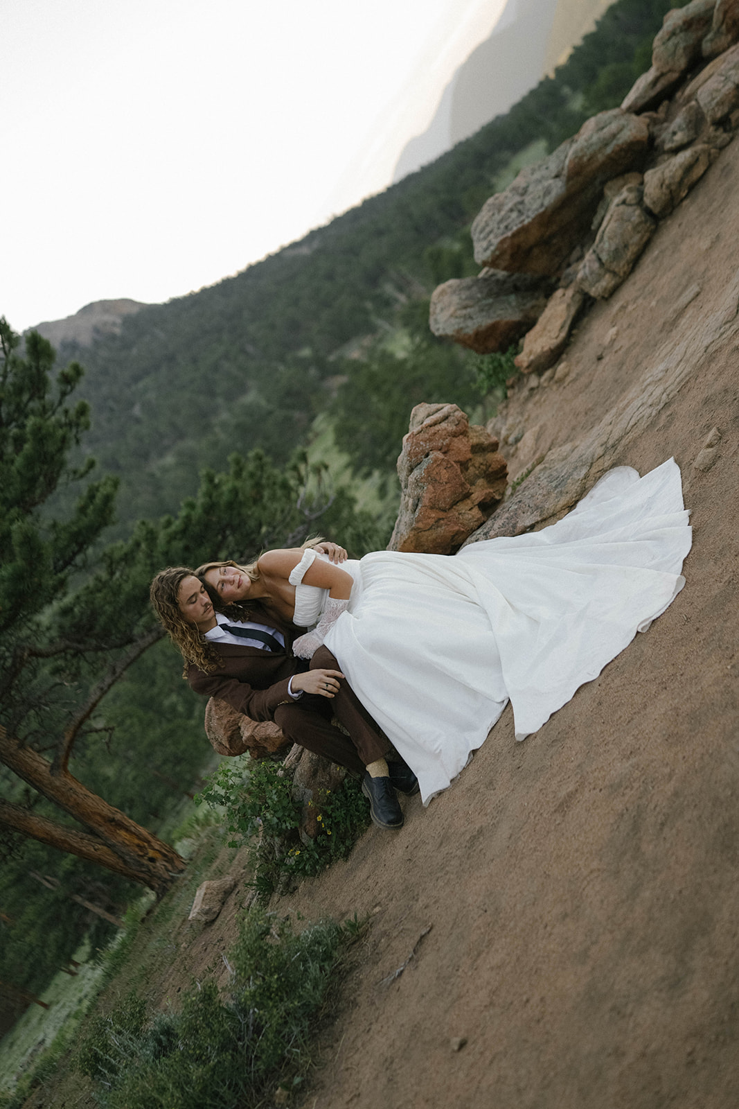 Close-up of bride and groom holding each other in soft mountain light, her lace gloves and off-the-shoulder gown glowing during their rocky mountain national park elopement.
