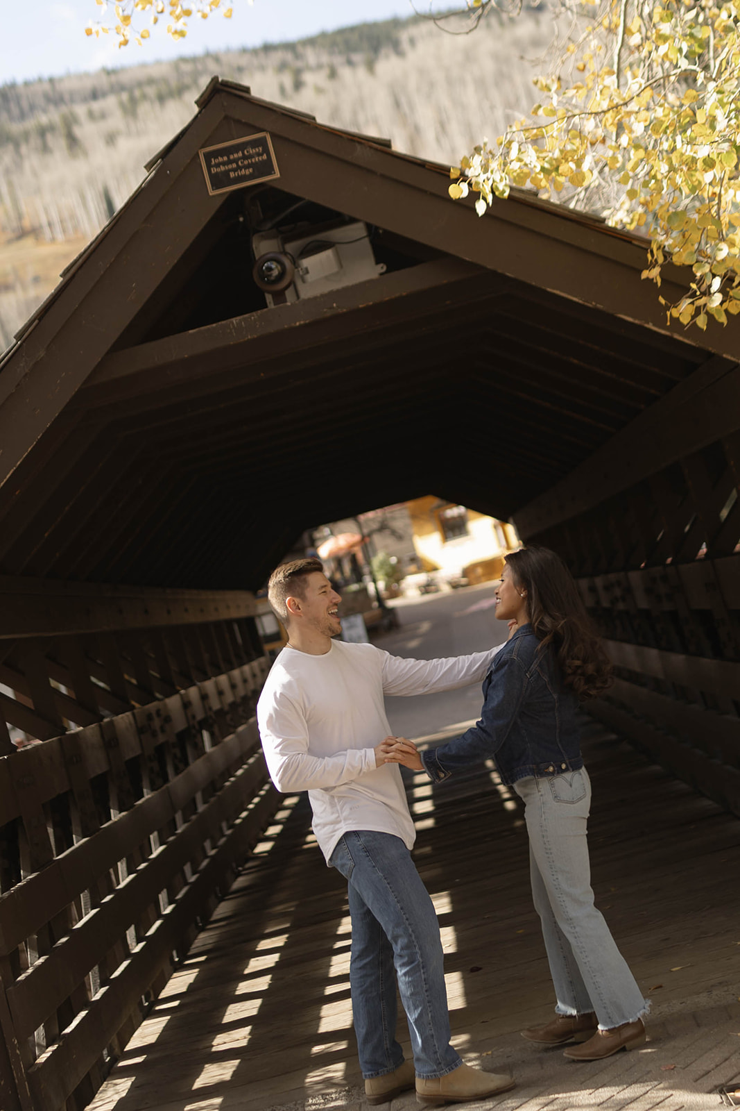 Intimate engagement photo of a couple kissing while holding black hats, framed by alpine architecture in vail village, colorado.
